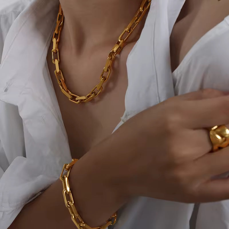 Gold chain necklace, bracelet, and ring worn by a person in a white shirt.
