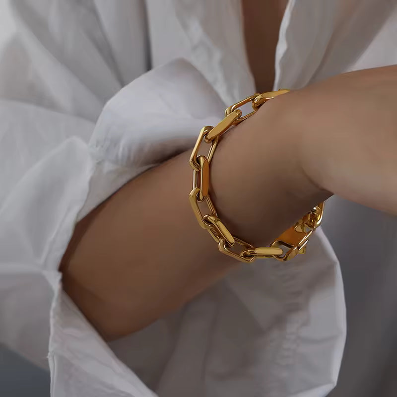 Gold chain bracelet on a wrist with a white shirt background