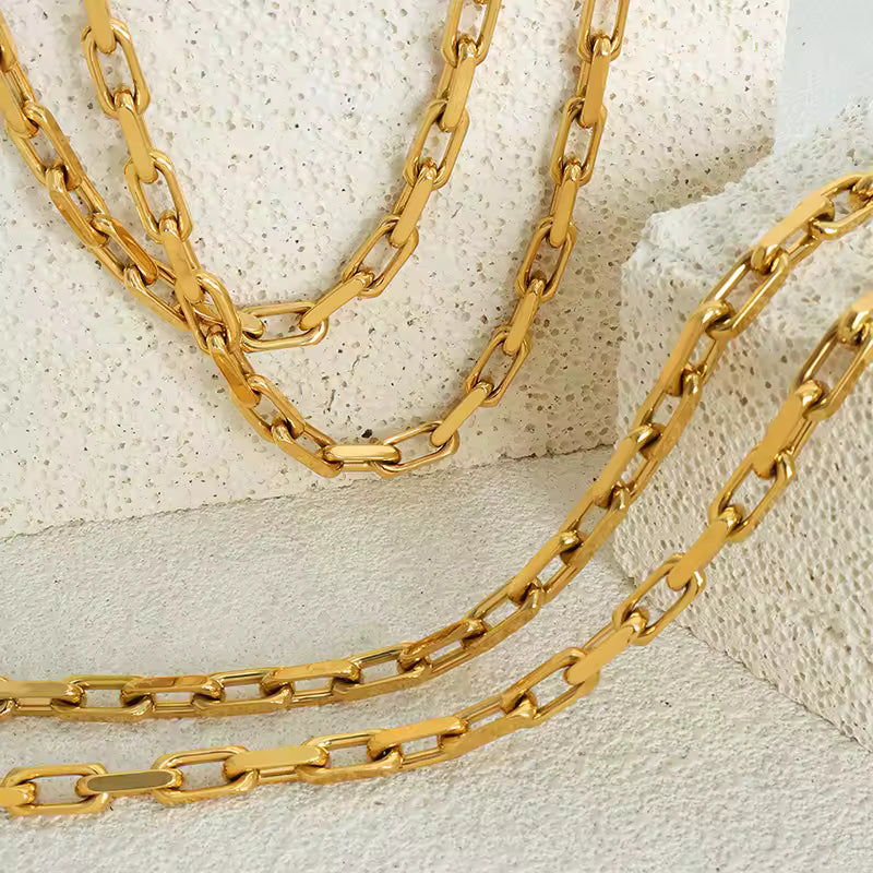 Two gold chain necklaces on a textured beige surface