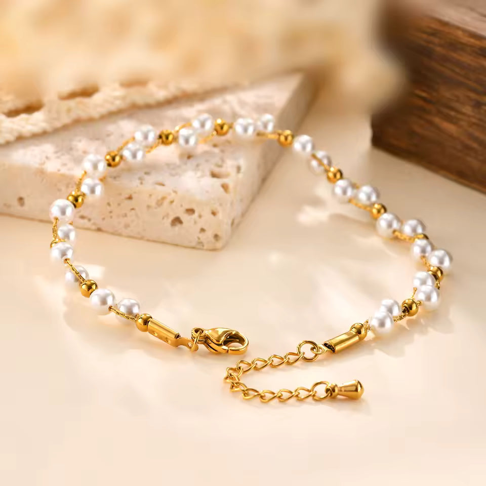 Gold and pearl bracelet on a beige surface with a wooden block in the background