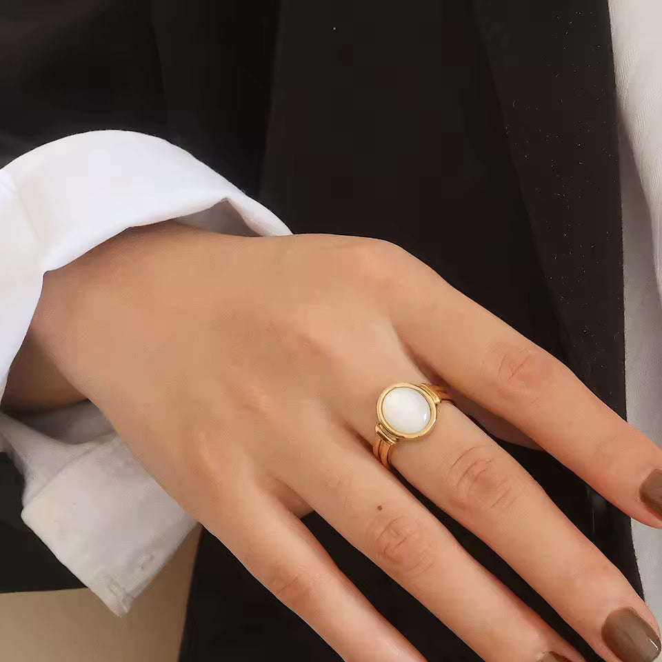 Hand wearing a gold ring with a white stone, against a black background