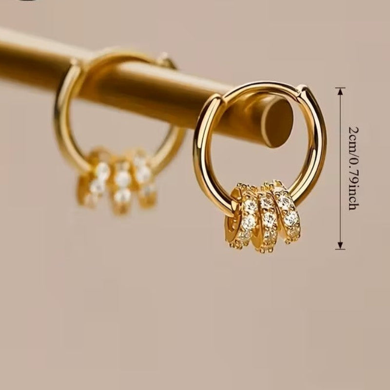 Gold hoop earrings with embedded stones on a beige background