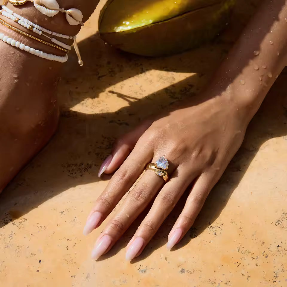 Hand wearing a gold ring with a clear stone on a textured surface