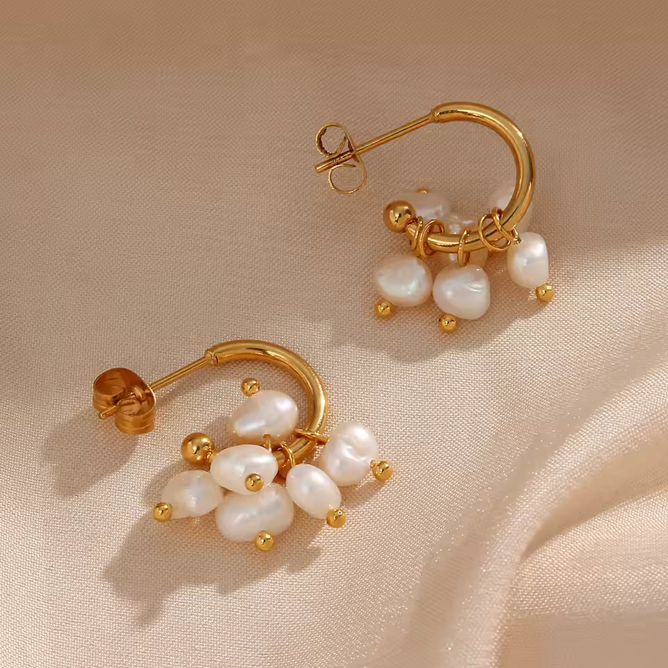 Gold hoop earrings with pearl drops on a beige fabric background
