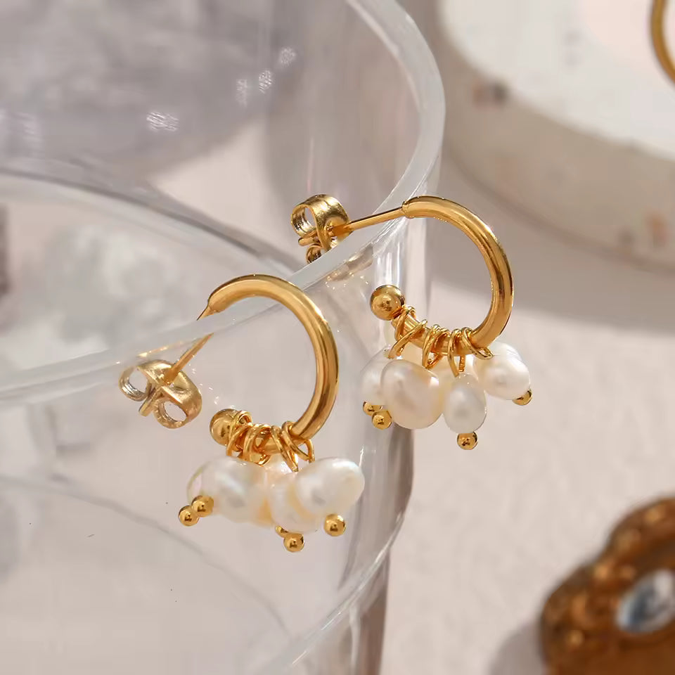Gold hoop earrings with pearl drops on a clear stand.
