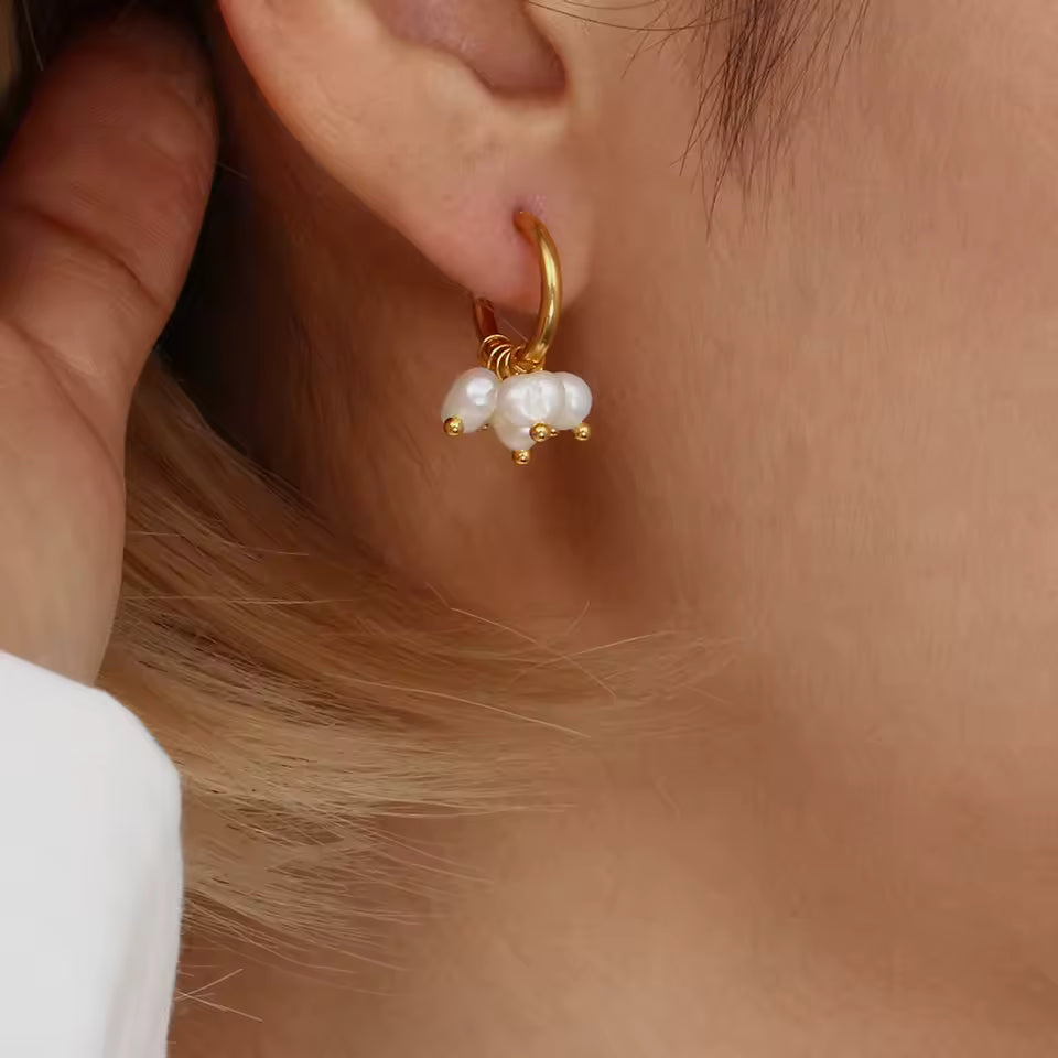 Gold hoop earring with pearl drops worn by a person.