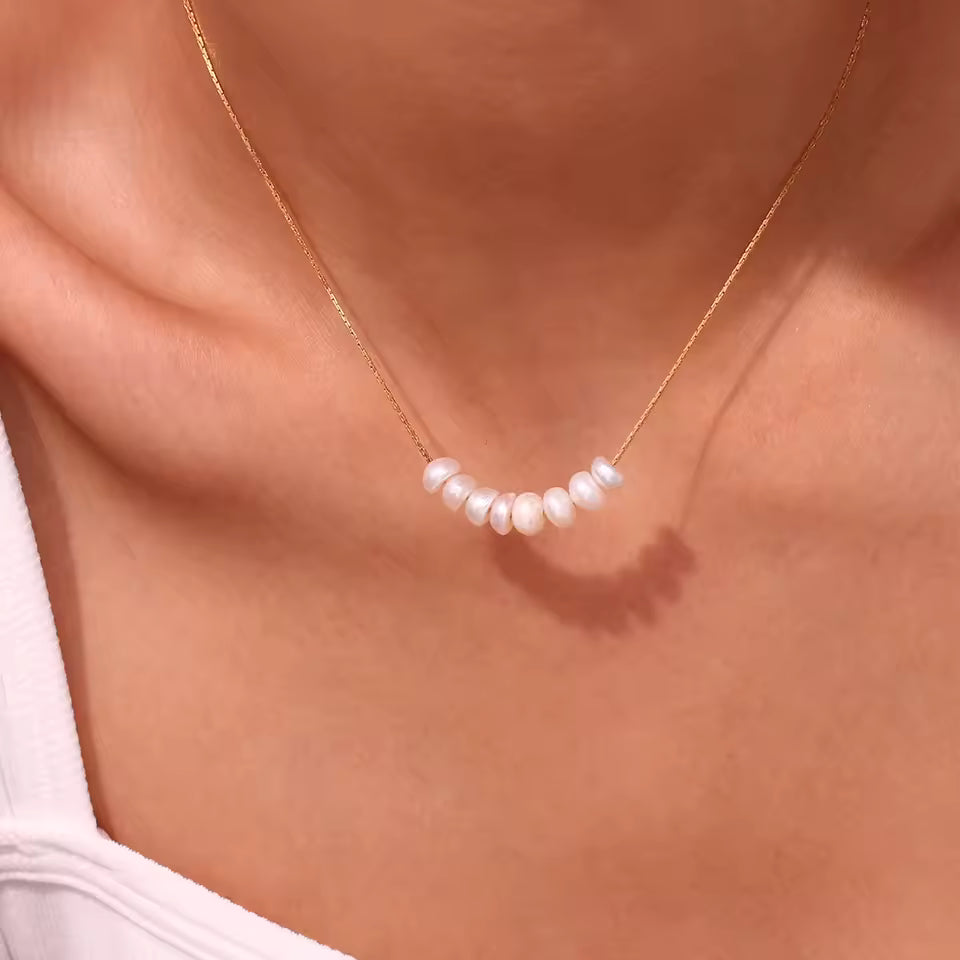 Pearl necklace on a person wearing a white top against a neutral background