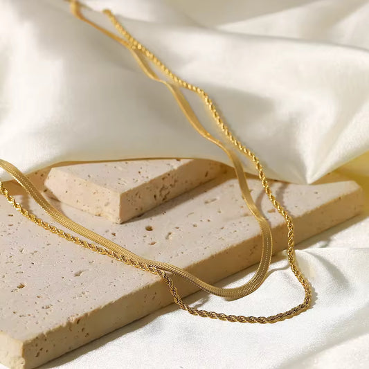 Gold chain draped over rectangular beige stones on a white fabric background