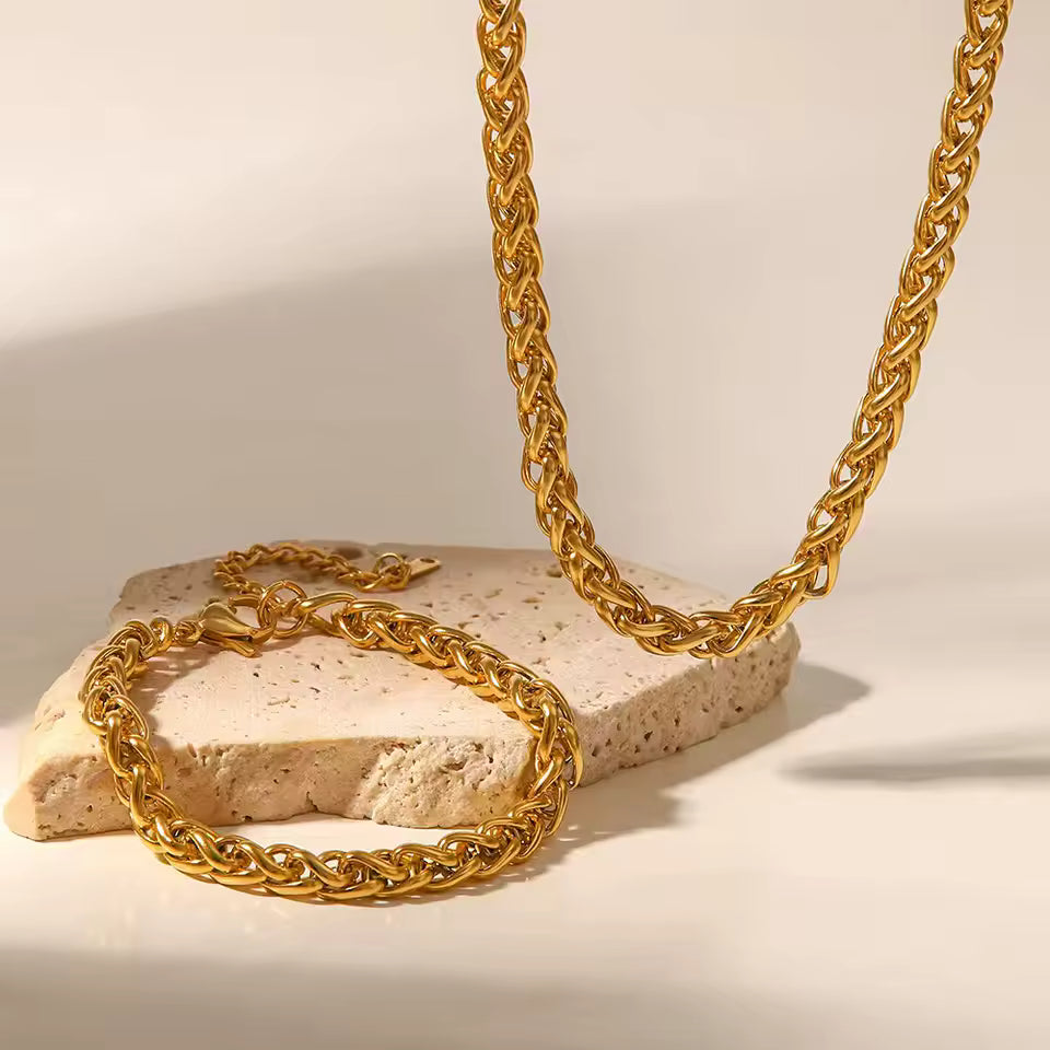 Gold chain necklace and bracelet on a textured stone surface with a neutral background