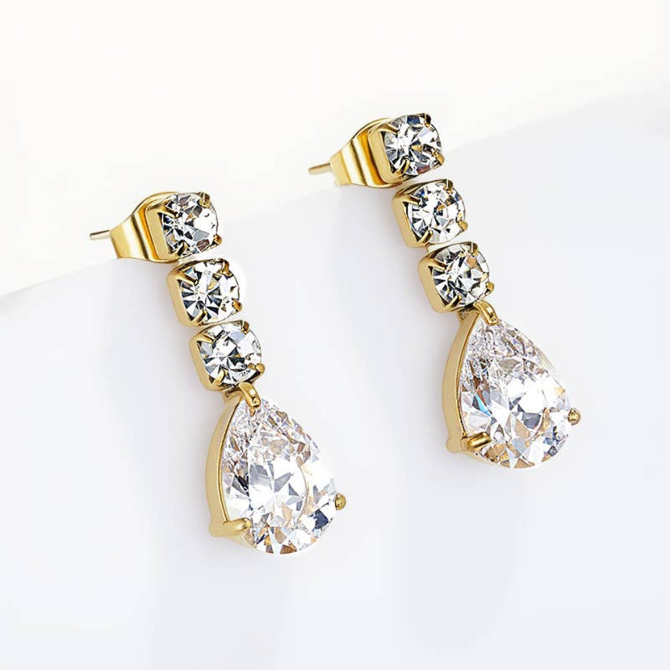 A pair of gold drop earrings featuring a vertical stack of clear teardrop and round crystals, with a larger teardrop crystal hanging at the bottom, displayed on a clean white surface.