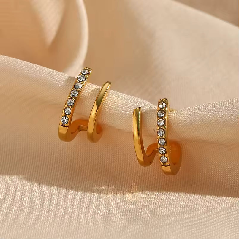 Gold hoop earrings with embedded diamonds on a beige fabric background