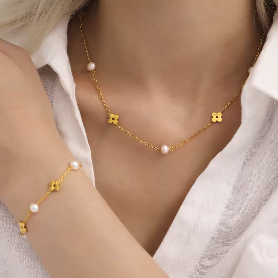 Gold necklace and bracelet with floral designs and freshwater pearls on a person wearing a white shirt.