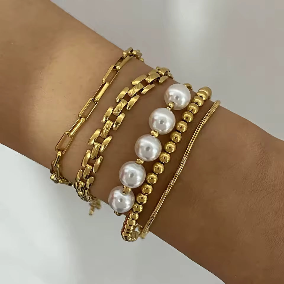 Gold and pearl bracelet set on a wrist against a neutral background