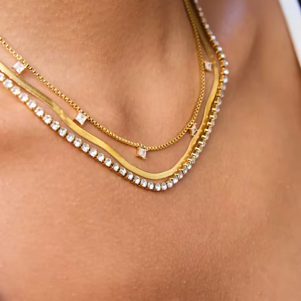 Close-up of a person wearing multiple gold necklaces with small gemstones on a light skin background.