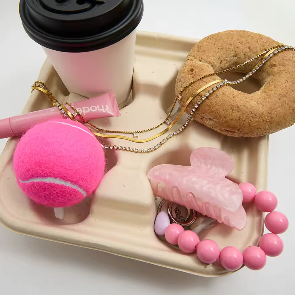 Pink tennis ball, donut, and other items on a tray with a white background