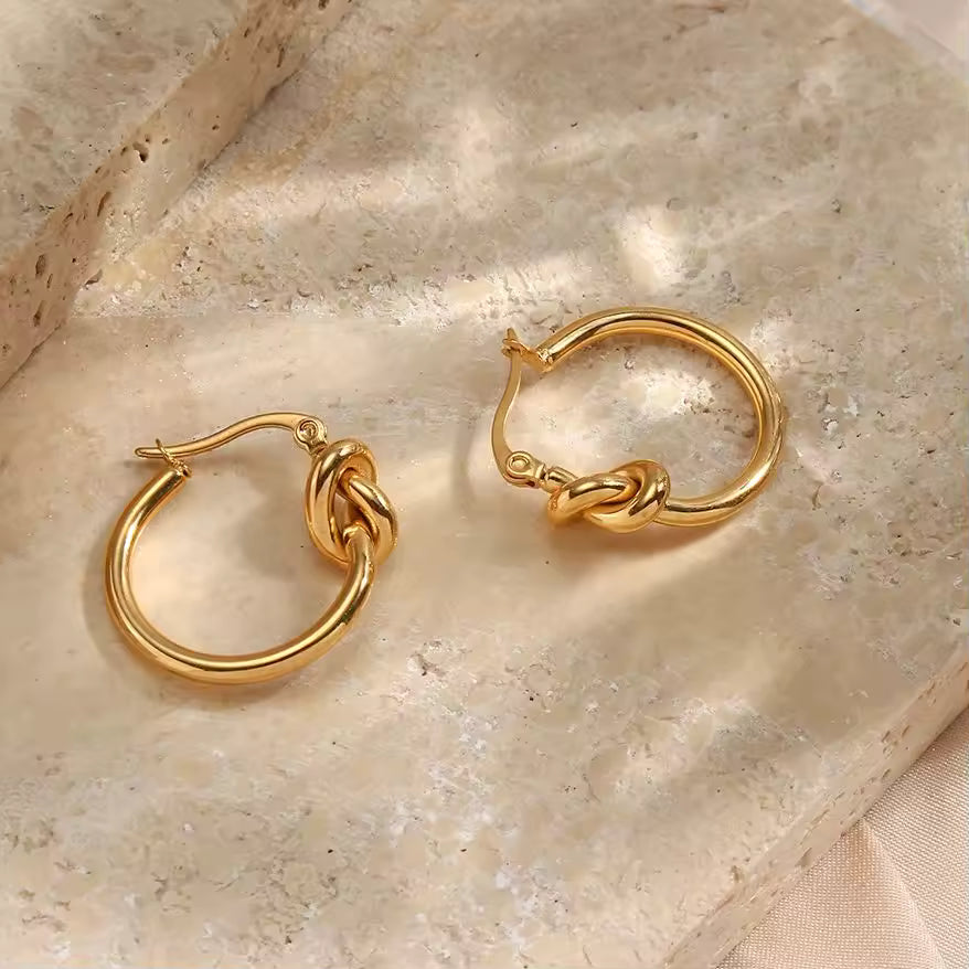 Pair of gold hoop earrings on a textured beige surface