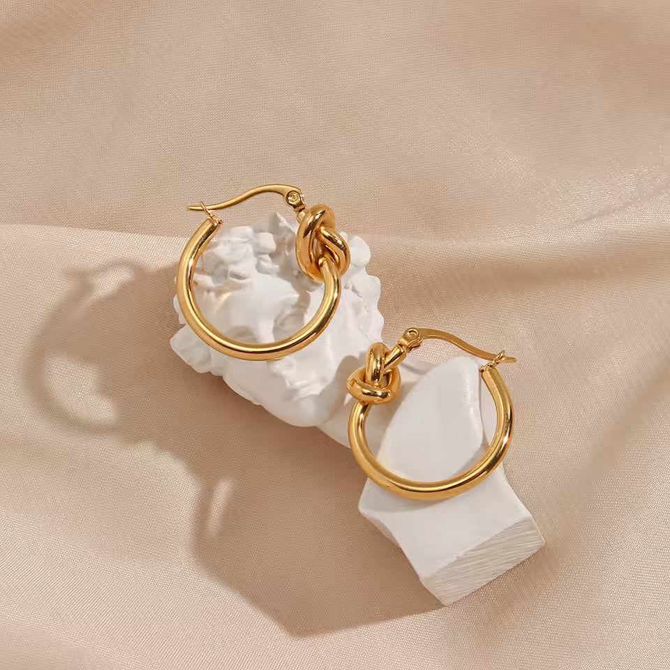 Gold hoop earrings with a white stone on a beige fabric background