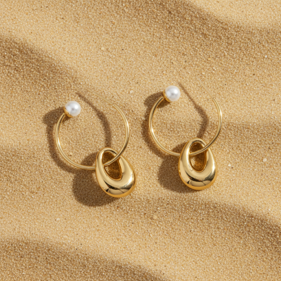 Gold hoop earrings with pearl accents on a sandy background