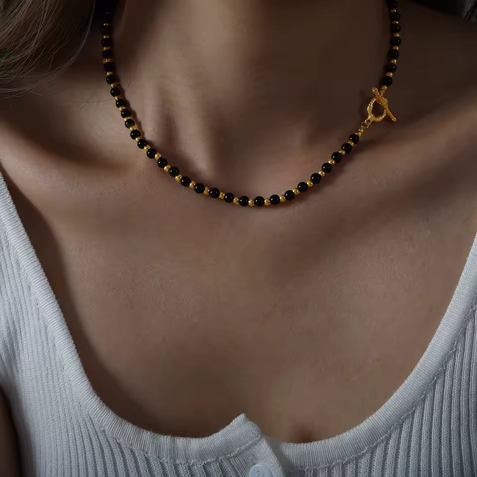 Necklace with black and gold beads on a person wearing a light gray top.
