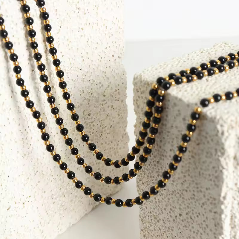 Black and gold beaded necklace on a textured white surface