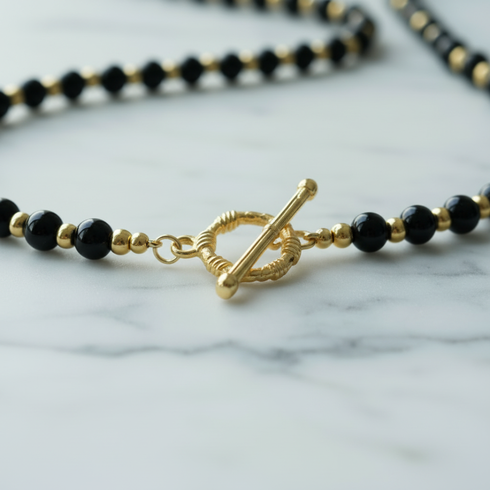 Black beaded necklace with a gold clasp on a marble surface