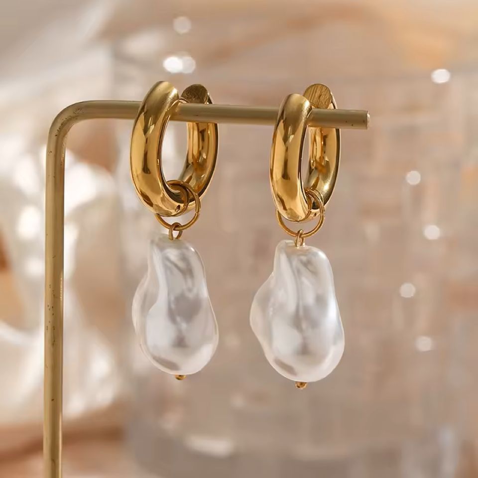 Gold hoop earrings with white pearl drops on a blurred background
