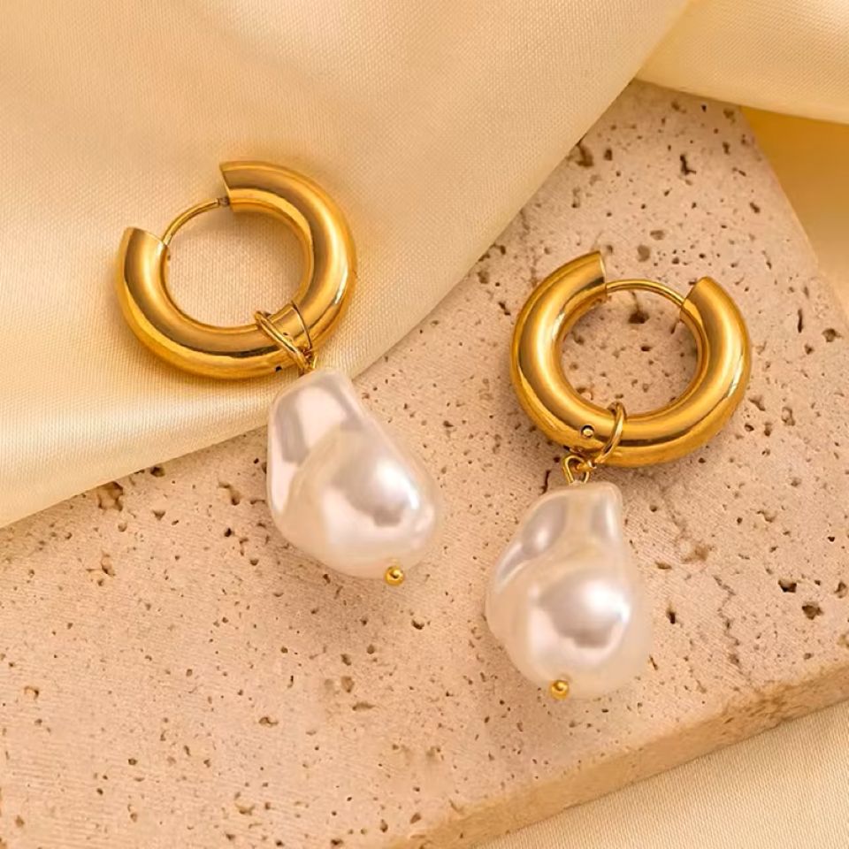 Gold hoop earrings with pearl drops on a textured beige surface