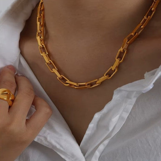Gold chain necklace worn by a person with a white garment and gold ring.
