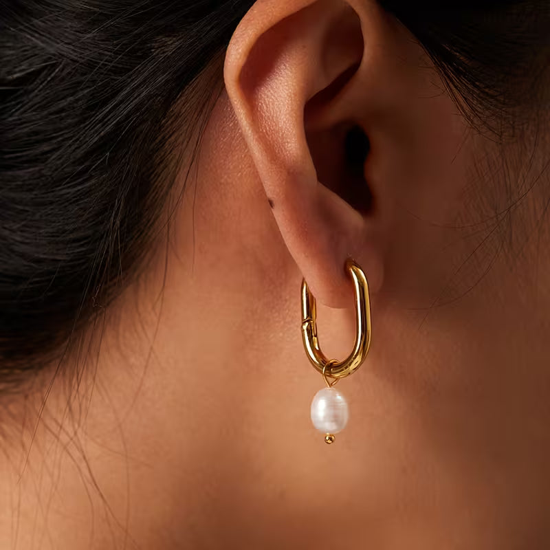 Gold hoop earring with a pearl drop worn by a person.