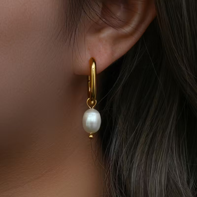 Gold hoop earring with a pearl drop worn by a person with dark hair.