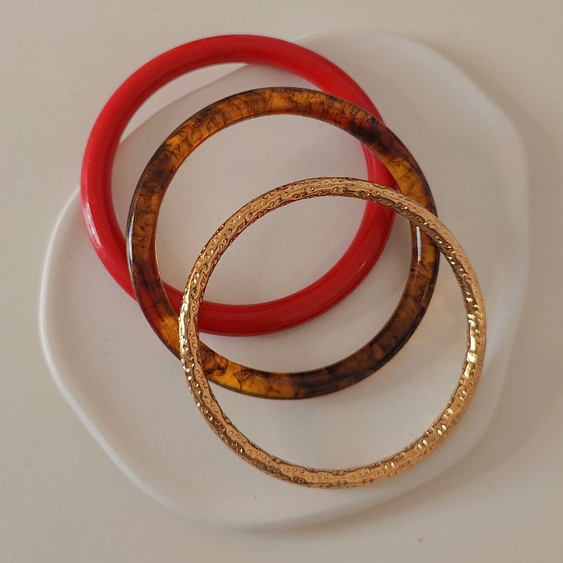 Three bracelets, one red and one tortoiseshell and one gold, on a white plate with white  background.