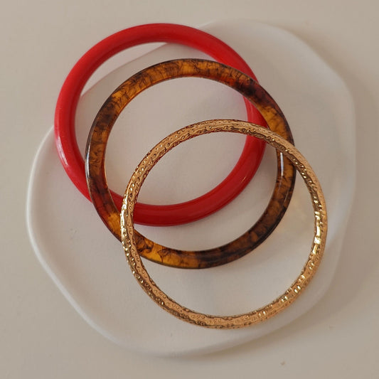 Three bracelets, one red and one tortoiseshell and one gold, on a white plate with white  background.