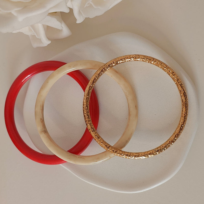 Three bracelets, one red, one off white and one gold on a white plate with white background