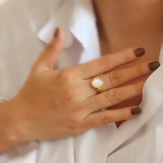 Hand wearing a gold ring with a white stone on a light background