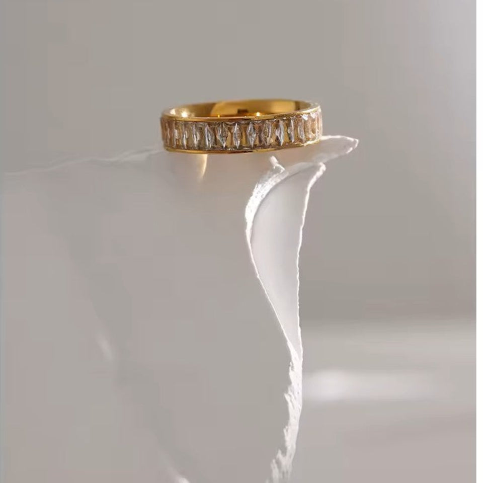 Gold ring with diamond accents on a white pedestal against a light gray background