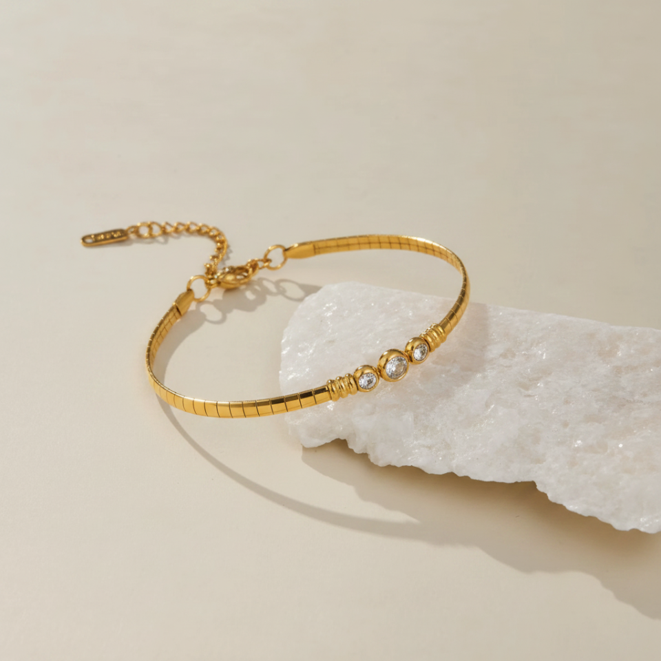 Gold bracelet with small stones on a textured beige surface