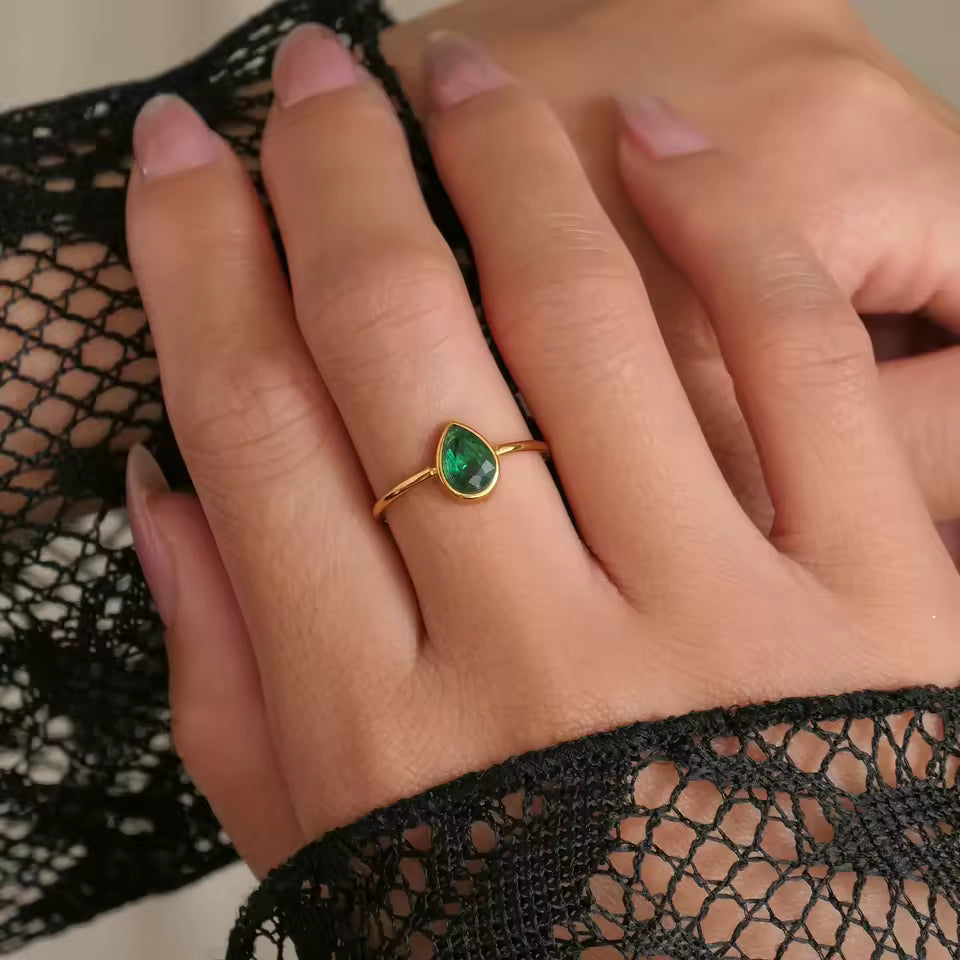 Hand wearing a gold ring with a green gemstone against black lace fabric