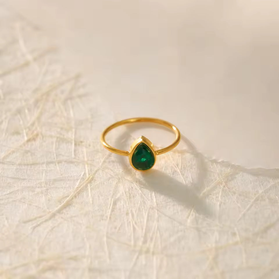 Gold ring with a green gemstone on a textured beige background