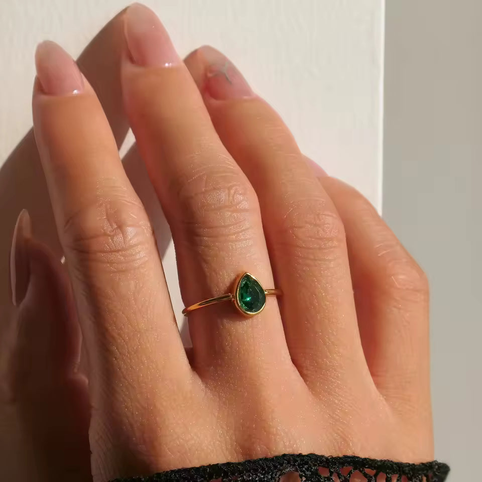 Hand wearing a ring with a green gemstone on a neutral background