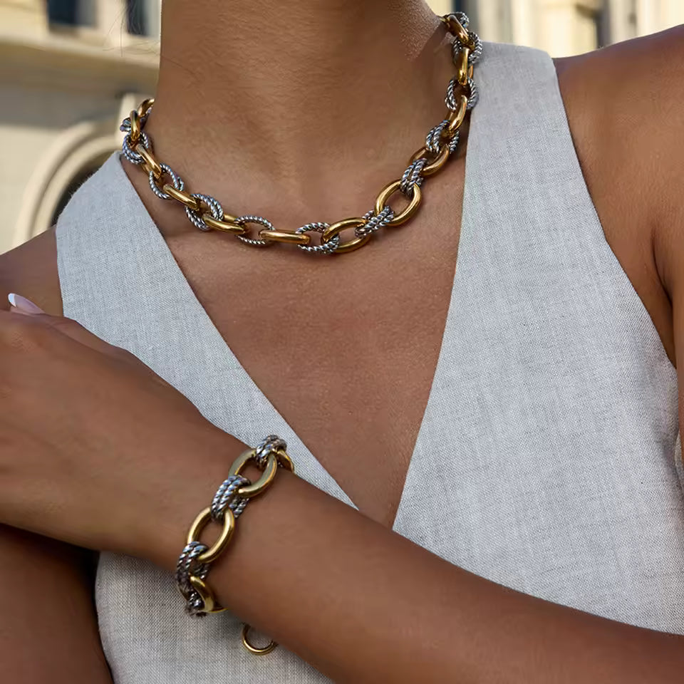 Gold chain necklace and bracelet on a person wearing a light gray sleeveless top.