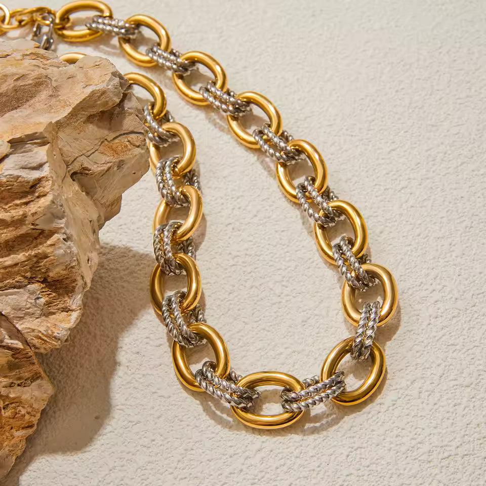 Gold chain necklace on a textured beige surface with a stone object.