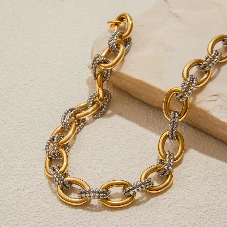 Gold and silver chain bracelet on a beige stone surface