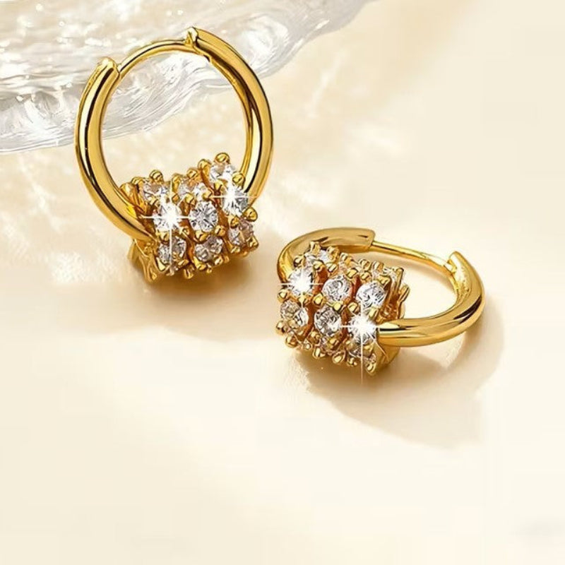 Gold hoop earrings with diamond-like stones on a beige background
