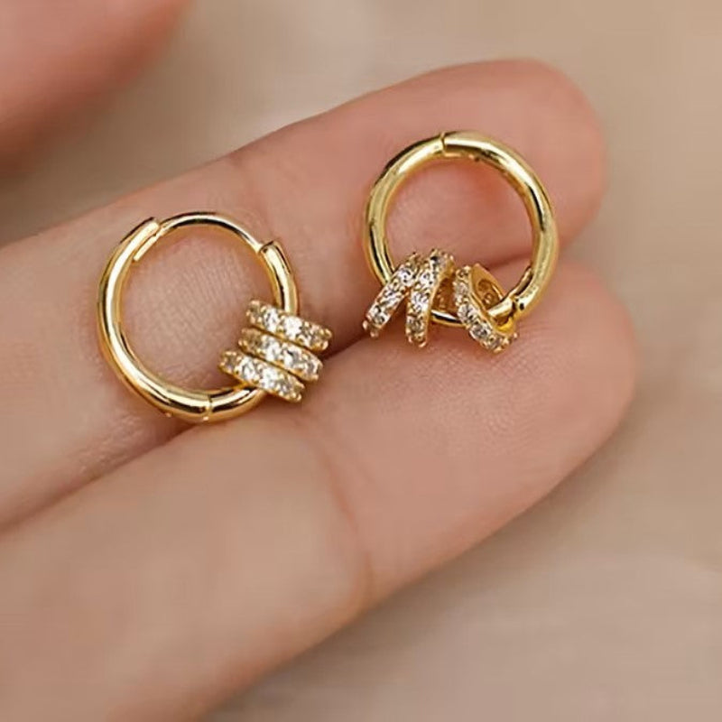 Gold hoop earrings with intricate designs on a hand against a beige background
