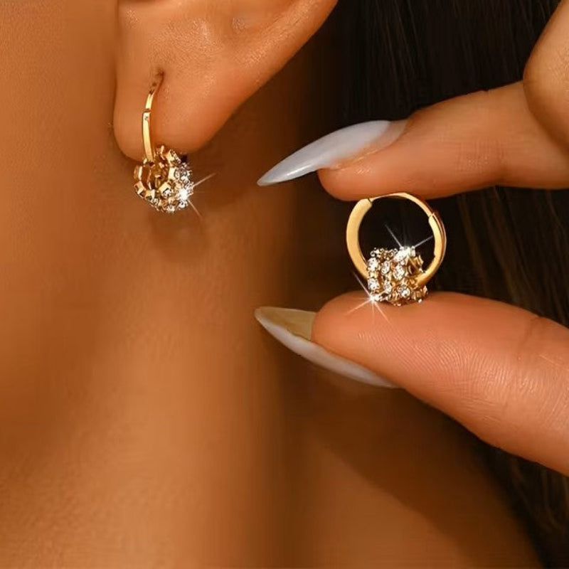 Gold hoop earrings with clear gemstones being worn and held by a person.