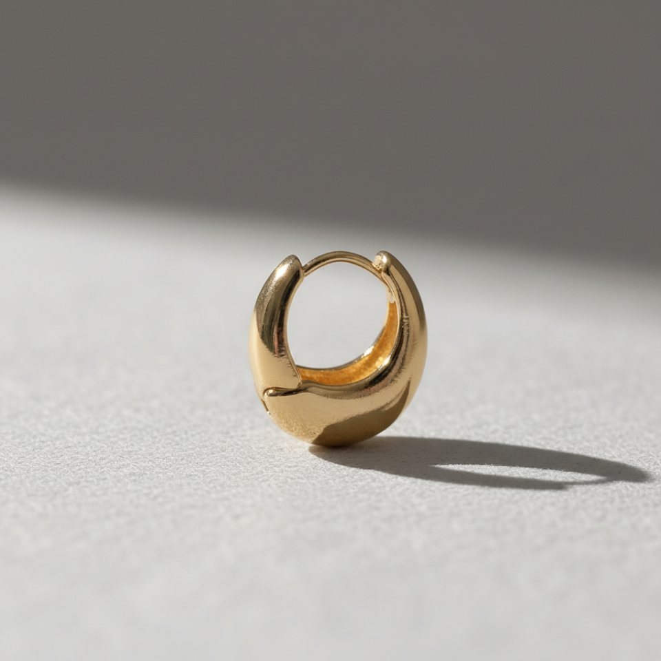 Gold hoop earring on a light gray surface with a neutral background