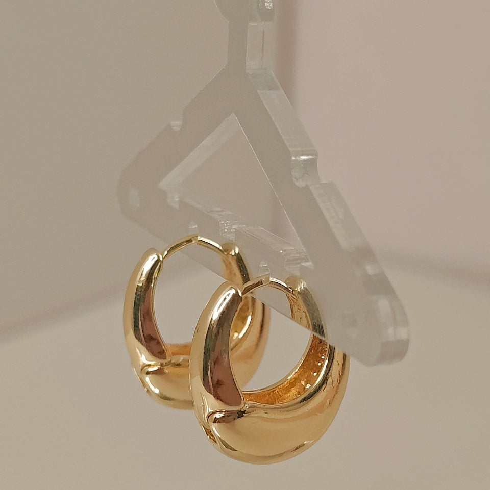 Gold hoop earrings on a clear hanger against a neutral background