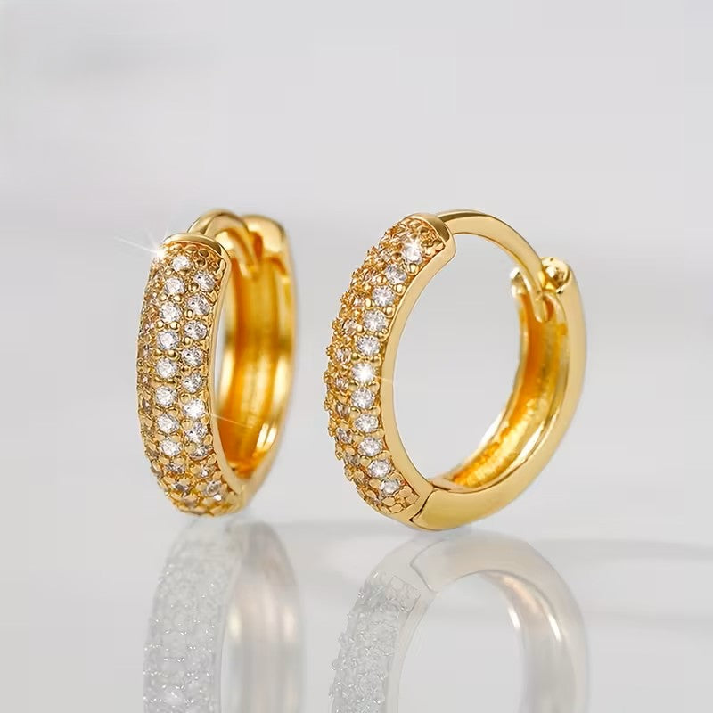 Gold hoop earrings with diamond accents on a reflective surface