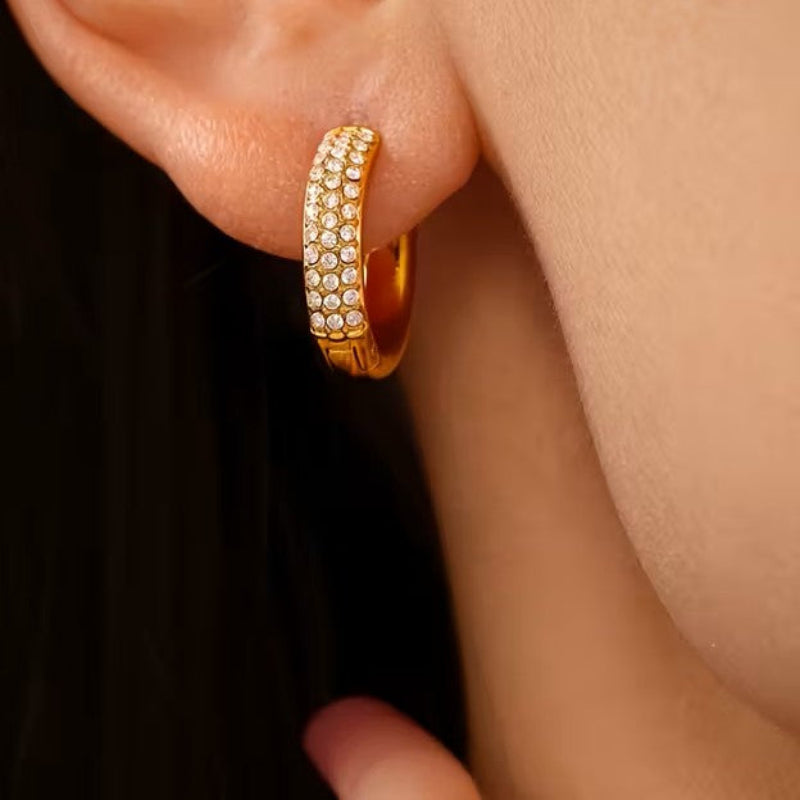 Gold hoop earring with embedded stones worn on an ear against a dark background