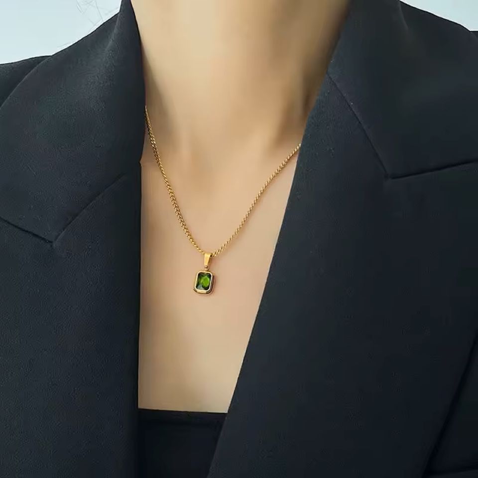 Gold necklace with a green gemstone pendant on a woman wearing a black blazer.
